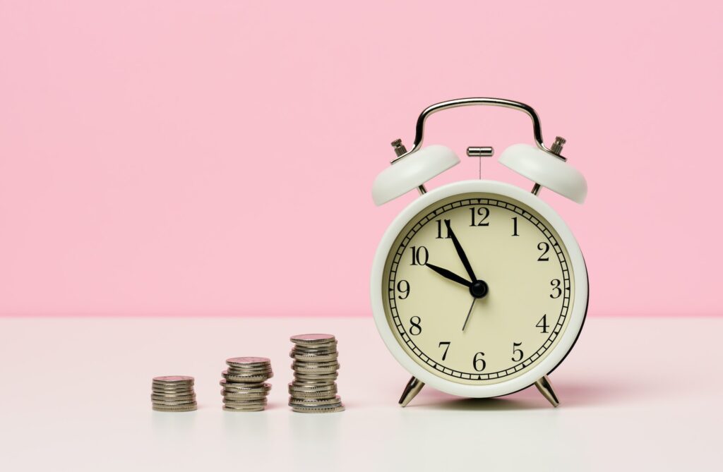 Stack of coins round white alarm clock on the table. The concept of time is money